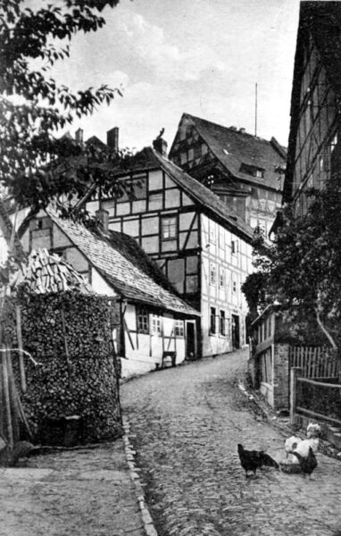 Der MühlenwegDer Mühlenweg ist der ursprüngliche Ortseingang von Norden in den Ort. Der anstrengende Anstieg aus der Niederung des Wesertals hinauf zum Bergsporn mit den einstigen Amtsgebäuden der Burg bzw. den Verwaltungsgebäuden wurde mit dem romantischen Blick über das Flußtal während des Aufstiegs belohnt. Hatte man den Mühlenweg erklommen, befand man sich auf dem Platz vor dem Amtshaus mit Ölmühle. Von hieraus konnte man der Amtsstraße in Richtung Süden nach Holzminden folgen oder sich - mit weiterem Anstieg - in die Burgstraße, der Hauptgeschäftsstraße des Ortes, begeben. Alle drei Fotos rechts zeigen das Erscheinungsbild des Mühlenwegs mit Blick auf die damaligen Amtsgebäude im unteren Teil der Burganlage. Leider sind diese Gebäude heute nicht mehr erhalten:
Im April 1945 wurden diese Gebäude weitestgehend zerstört, so dass heute lediglich der Steinbogen des Renaissanceportals, das den Haupteingang zum Amtshaus bildete, sowie dessen einstige, untere Geschosse des Westflügels - in dem u.a. das örtliche Gefängnis untergebracht war - erhalten geblieben sind.
Weitere Gebäude wurden im Bereich des Mühlenweges sowie der Unterburg in der zweiten Hälfte des letzten Jahrhunderts errichtet, wobei durch umfangreiche Um- und Neubaumassnahmen im Bereich der Unterburg zum Jahrtausendwechsel eine Erneuerung und Ergänzung dieses Bereiches erfolgen konnte.
Die heutige Bebauungsstruktur im Bereich des Mühlenwegs folgt der sich somit als persistent erweisenden historischen Bebauung in Orientierung, Größe und Ausrichtung der Gebäude, so dass man noch heute einen Eindruck des historischen Mühlenwegs erhalten kann.